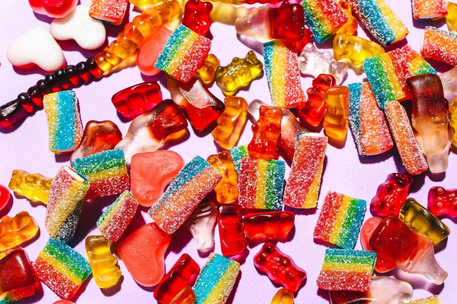 Colorful mix of gummy candies including bears and rainbow strips on a vibrant purple backdrop.
