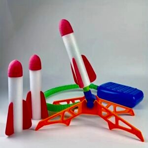image 9A colorful foam rocket launcher toy set featuring three white foam rockets with red fins and pink tips, an orange plastic launch stand, a green flexible hose, and a blue foot pump stomp pad.
