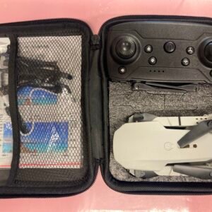 An open black travel case containing a foldable gray gesture control drone, a dedicated remote controller, and a mesh pocket with an instruction manual and USB charging cable.