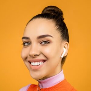 Bright and cheerful portrait of a young woman smiling with wireless earphones, against an orange background.