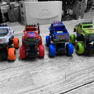Four high-speed electric music car toys in white, red, blue, and neon green with gilded paint accents, oversized textured tires, and inertia drive.