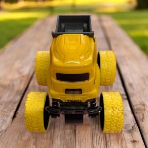 Front view of a yellow inertia-powered stunt toy truck with oversized textured yellow tires, parked on a wooden surface with a blurred outdoor background.